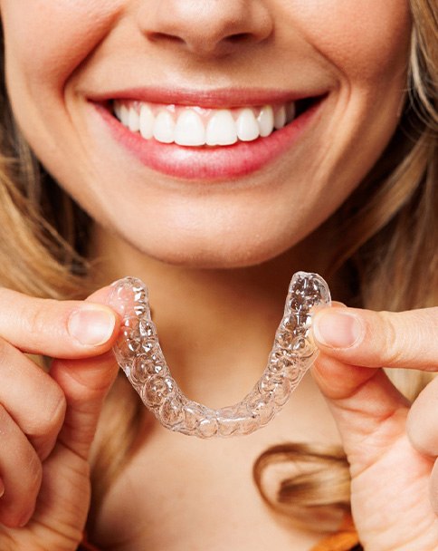 Nose-to-neck view of smiling woman holding clear aligner