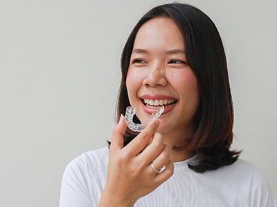 Smiling patient holding clear aligner