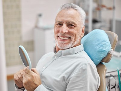 patient smiling while holding implant mirror