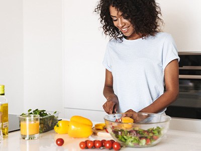 Woman at kitchen counter cutting vegetables for salad
