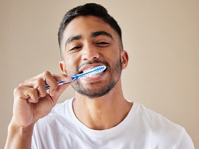 Man brushing teeth with standard toothbrush with tan background