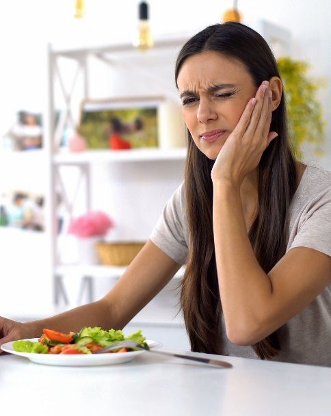 Woman sitting at table with salad and holding her cheek in pain