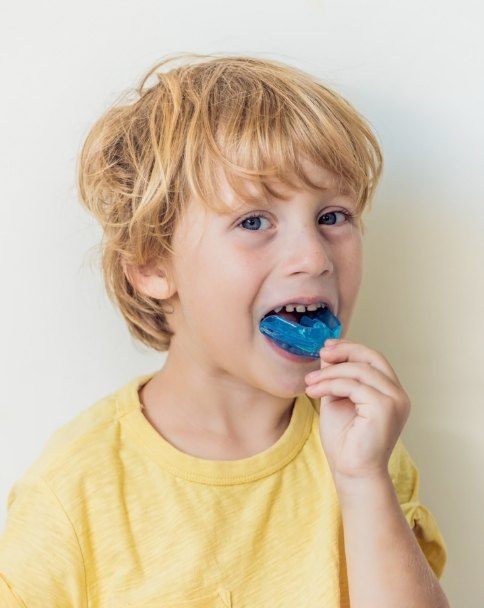 Young boy placing blue athletic mouthguard into his mouth
