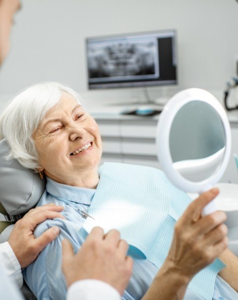 Senior dental patient admiring her smile in mirror