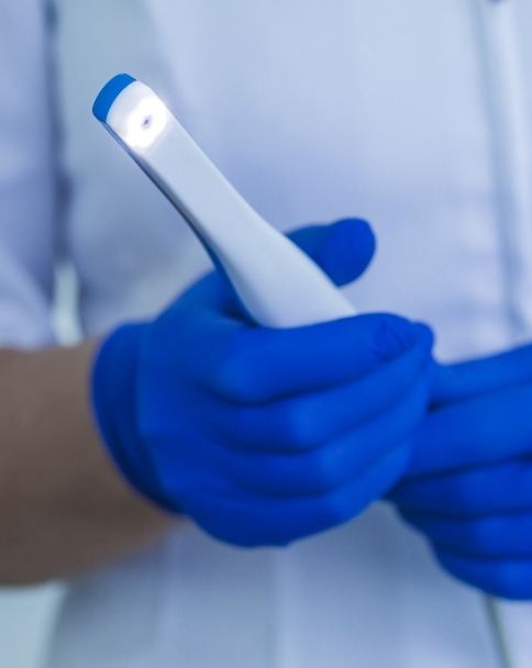 Two gloved hands holding a thin white intraoral camera