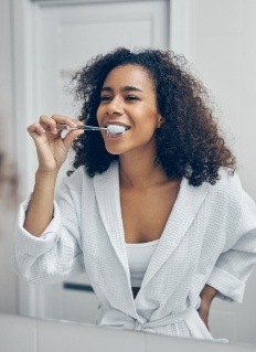 Woman in white bathrobe brushing her teeth