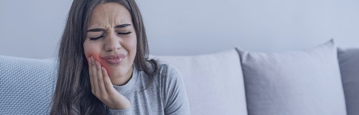 Woman sitting on couch holding her cheek in pain