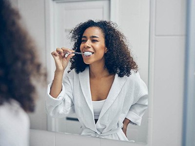 Woman smiling while brushing her teeth in bathroom