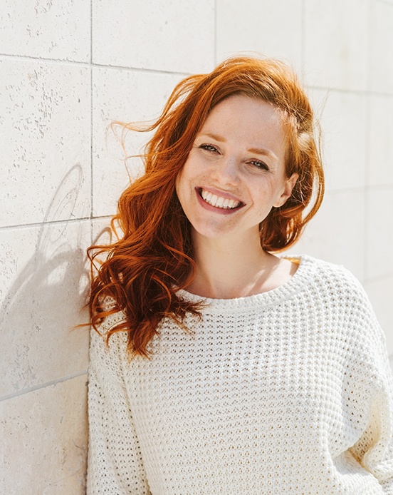Woman in sweater leaning against wall with brighter smile