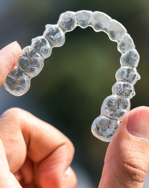 Hand holding an Invisalign clear aligner outdoors