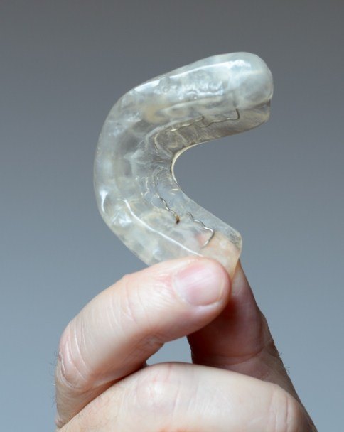 Hand holding a white nightguard for bruxism treatment