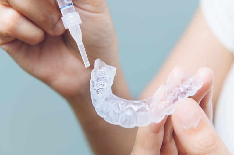 A woman holding a teeth whitening tray and bleaching gel